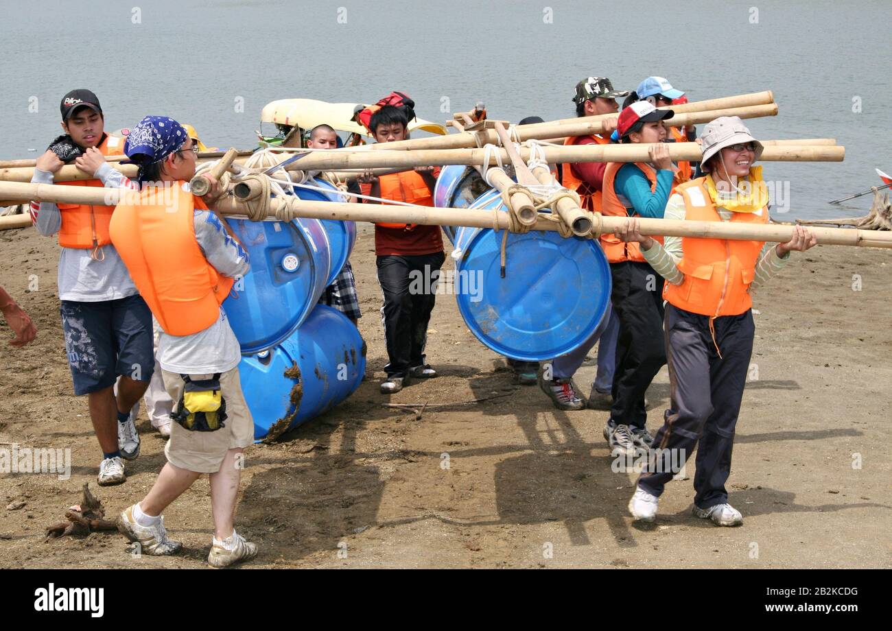 Un gruppo di persone portano una barca di emergenza che ha fatto di bastoni di bambù, barili di plastica e corde in un allenamento di sopravvivenza all'aperto. Foto Stock