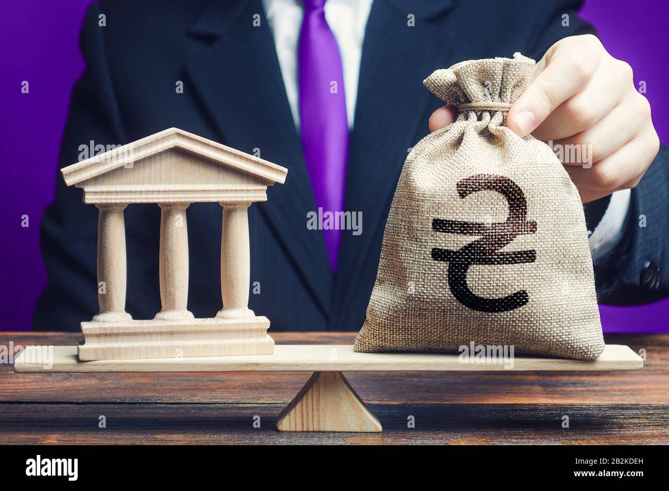Un uomo mette una borsa di denaro hryvnia ucraina su scale di fronte alla pubblica amministrazione o banca. Debito statale. Deficit di bilancio. Tasse di pagamento. Lobbyin Foto Stock