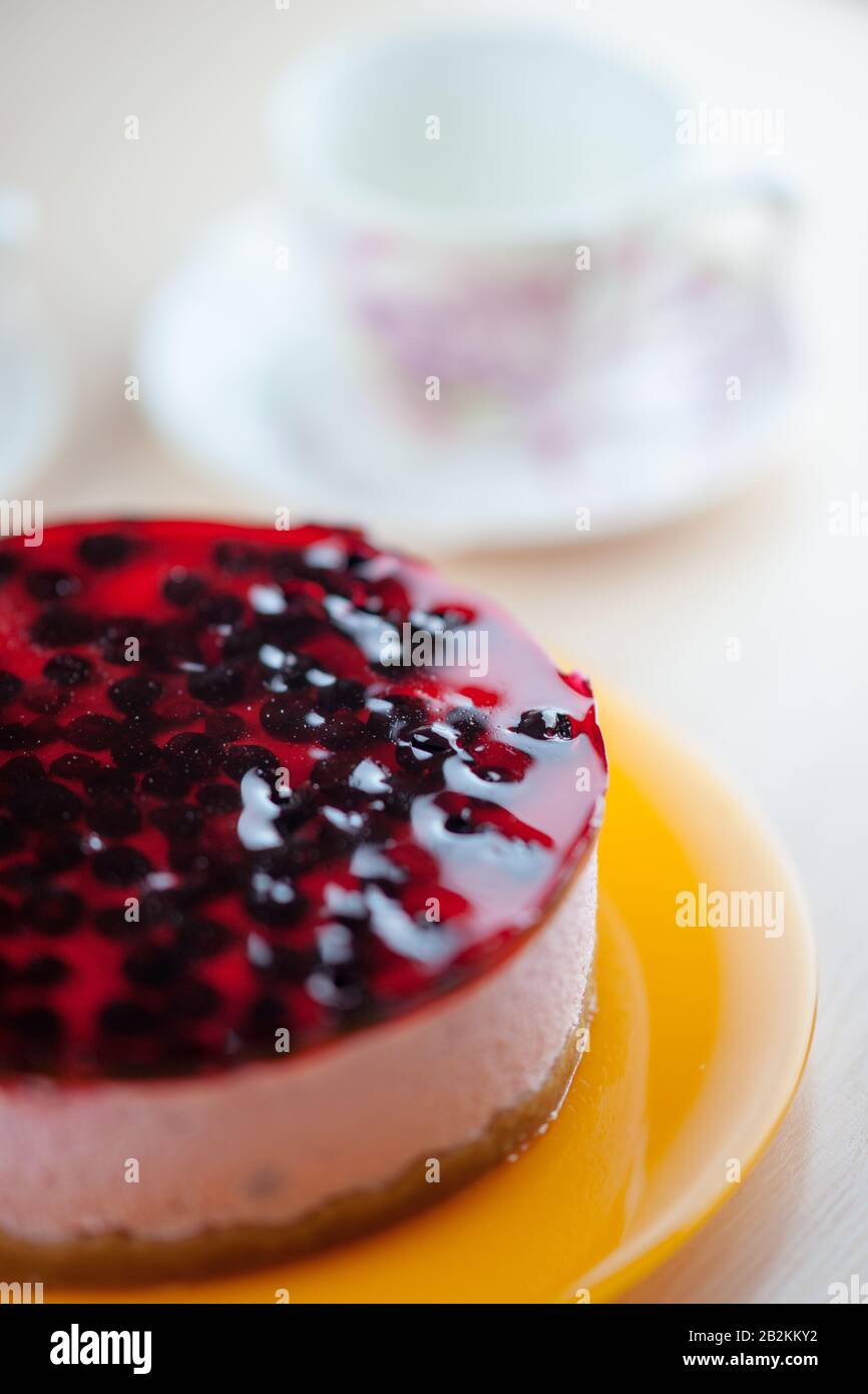 Cheesecake di ribes in un piatto di arancia. Su una tazza di fondo sfocata per il tè. Foto Stock