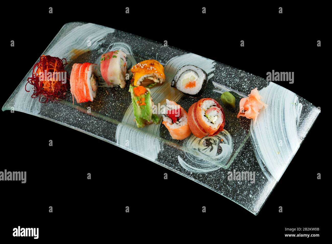 Una varietà di sushi roll sono disposti su un piatto rettangolare di vetro testurizzato con un design astratto bianco e nero. Il sushi comprende diversi tipi, come quelli avvolti in salmone, avocado e granchio Foto Stock