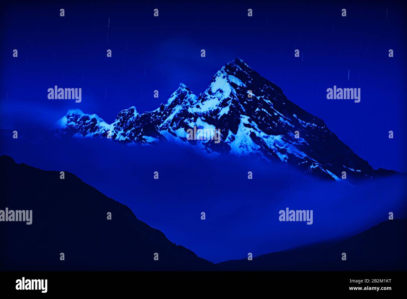 Una spettacolare vista notturna delle aspre vette innevate che si innalzano sopra un denso strato di nuvole. La scena è illuminata da una luce blu fredda, probabilmente luce di luna o luce notturna Foto Stock