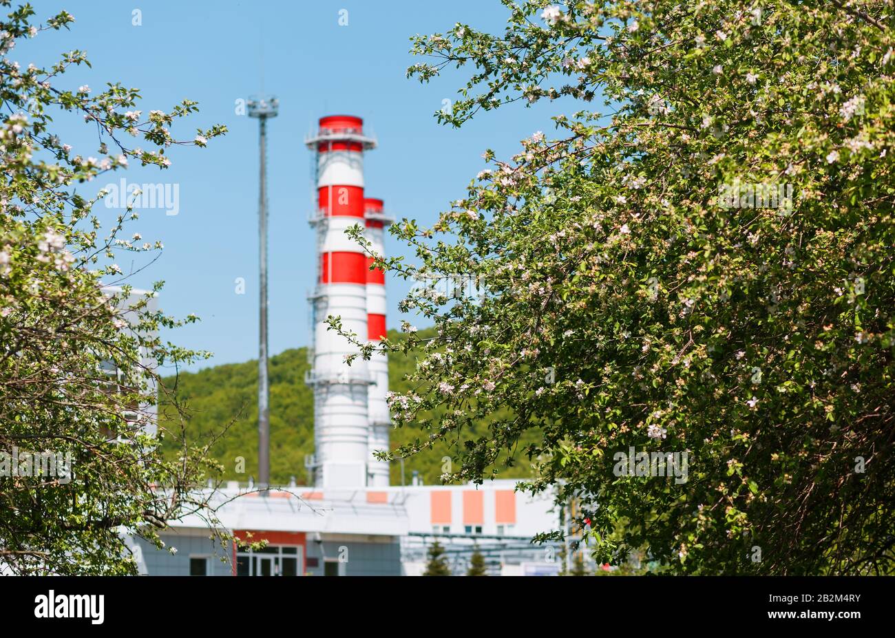 Turbina a gas centrale su gas naturale con camini di colore rosso-bianco contro il cielo blu nel frutteto di mele. Basse emissioni e problemi ambientali Foto Stock