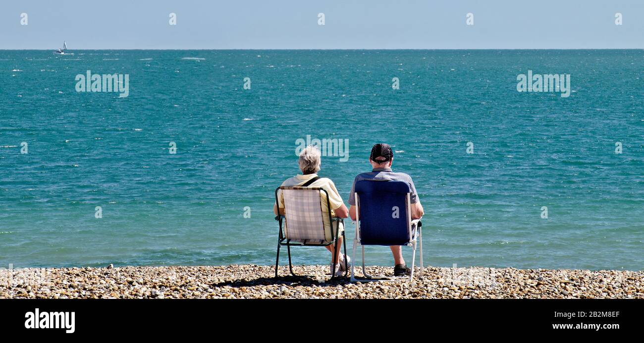 uomo e donna seduti sulle sedie a sdraio sulla spiaggia di ghiaia che si affaccia sul mare in una calda giornata di estati. Foto Stock