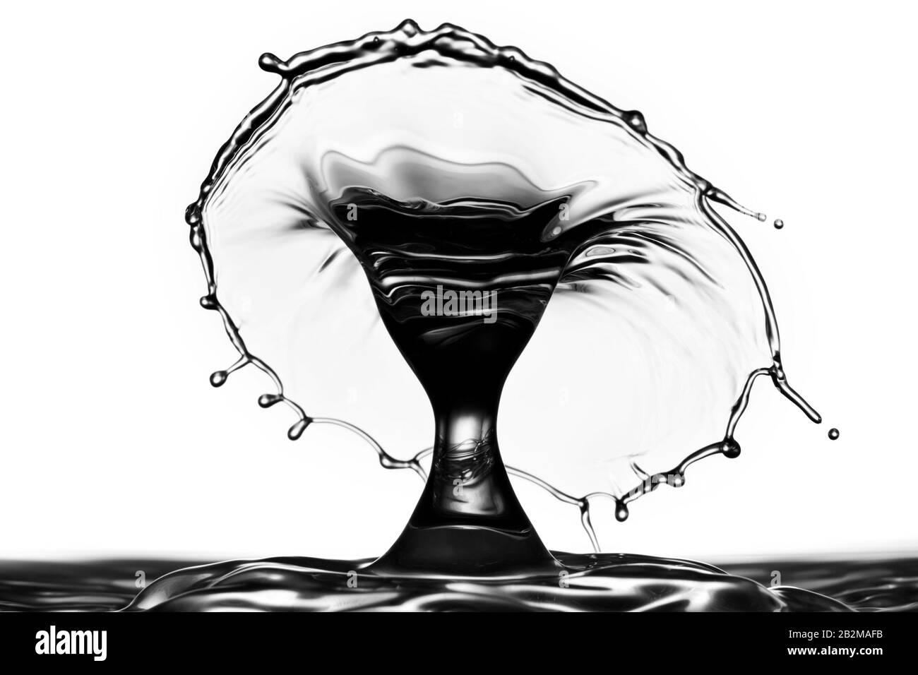 Una fotografia ad alta velocità cattura il momento in cui una goccia d'acqua colpisce una superficie liquida, formando uno spruzzo a forma di corona. L'immagine viene resa in monocromia, sottolineando il contrasto tra le aree scure Foto Stock