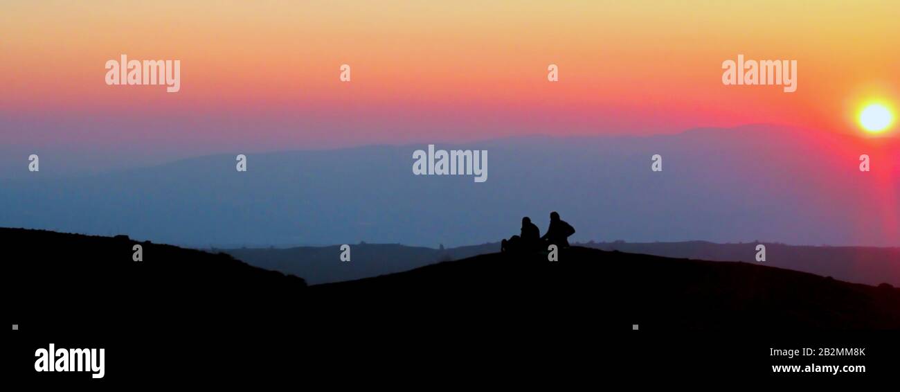 Una coppia seduta su una piccola collina si staglia contro un bel cielo serale al tramonto. Foto Stock