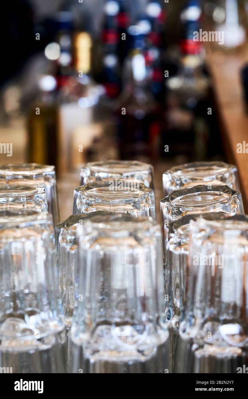 File di bicchieri in un bar in attesa di essere utilizzato. Sullo sfondo ci sono bottiglie di bevande alcoliche. Foto Stock