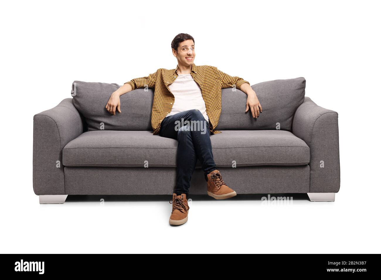 Giovane uomo seduto su un divano grigio isolato su sfondo bianco Foto Stock