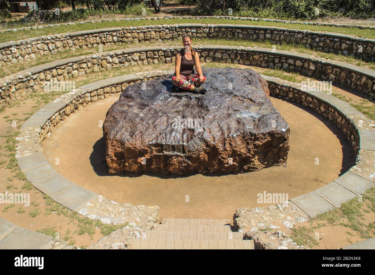 il meteorite più grande del mondo a Grootfontein, Namibia. Un pezzo enorme di ferro dallo spazio. Ragazza bianca turista seduto su un meteorite Foto Stock