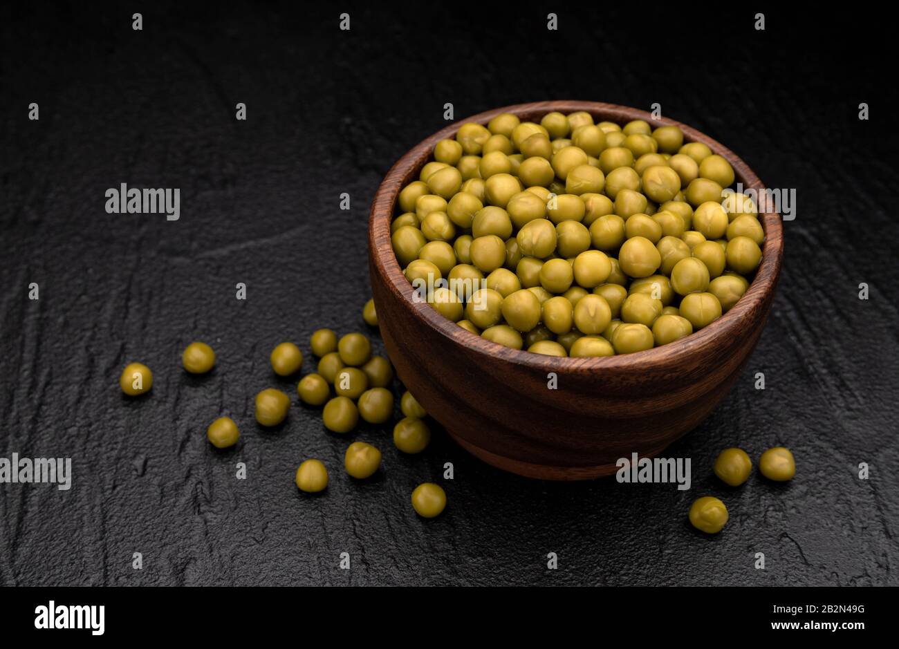 Mucchio di piselli verdi in scatola su sfondo nero Foto Stock