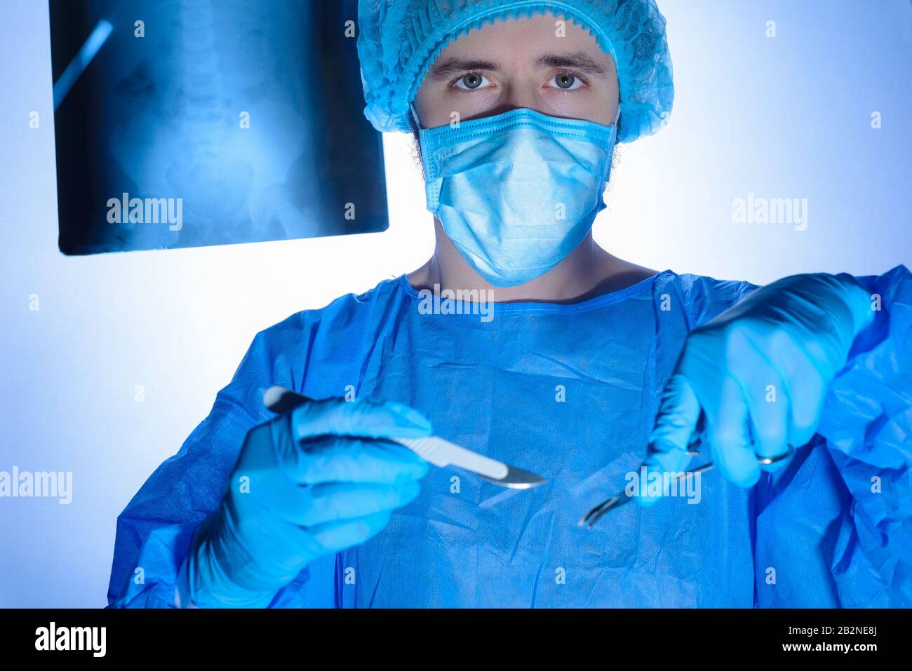 Ritratto di un chirurgo in abiti sterili, cappelli e maschere. Tenendo un bisturi e un supporto dell'ago con un ago, indirizzarli nella ferita chirurgica, p. Foto Stock