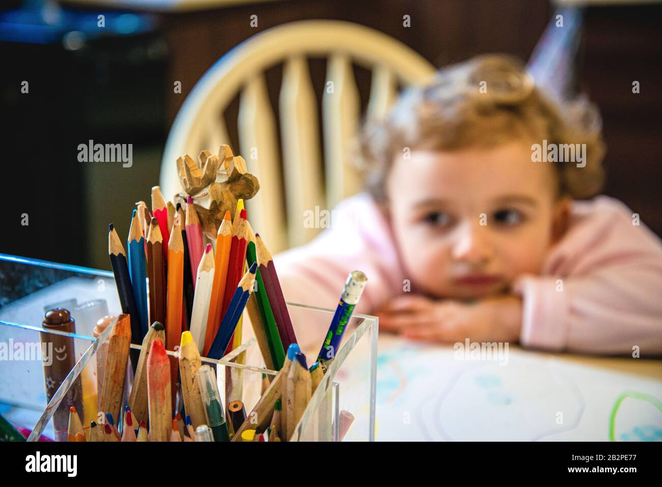 primo piano di plastica scatola a forma di supporto, con matite multicolore e pastelli, giovane ragazza guardando annoiato in background, fuori fuoco. Foto Stock