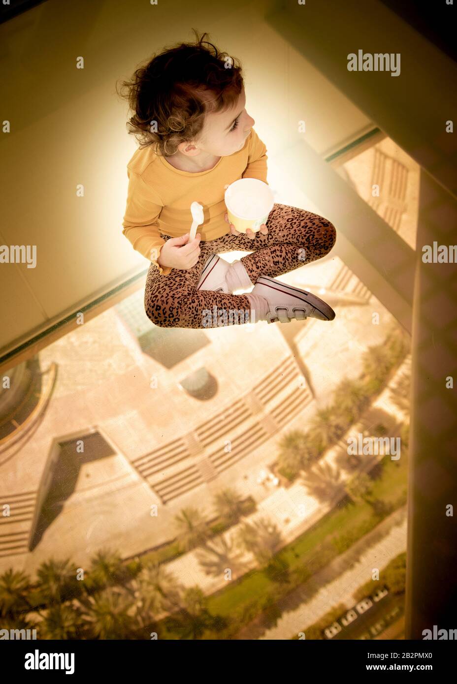 Bambino seduto a gambe incrociate su pavimento di vetro mangiare gelato nel Frame Building Dubai Emirati Arabi Uniti Foto Stock