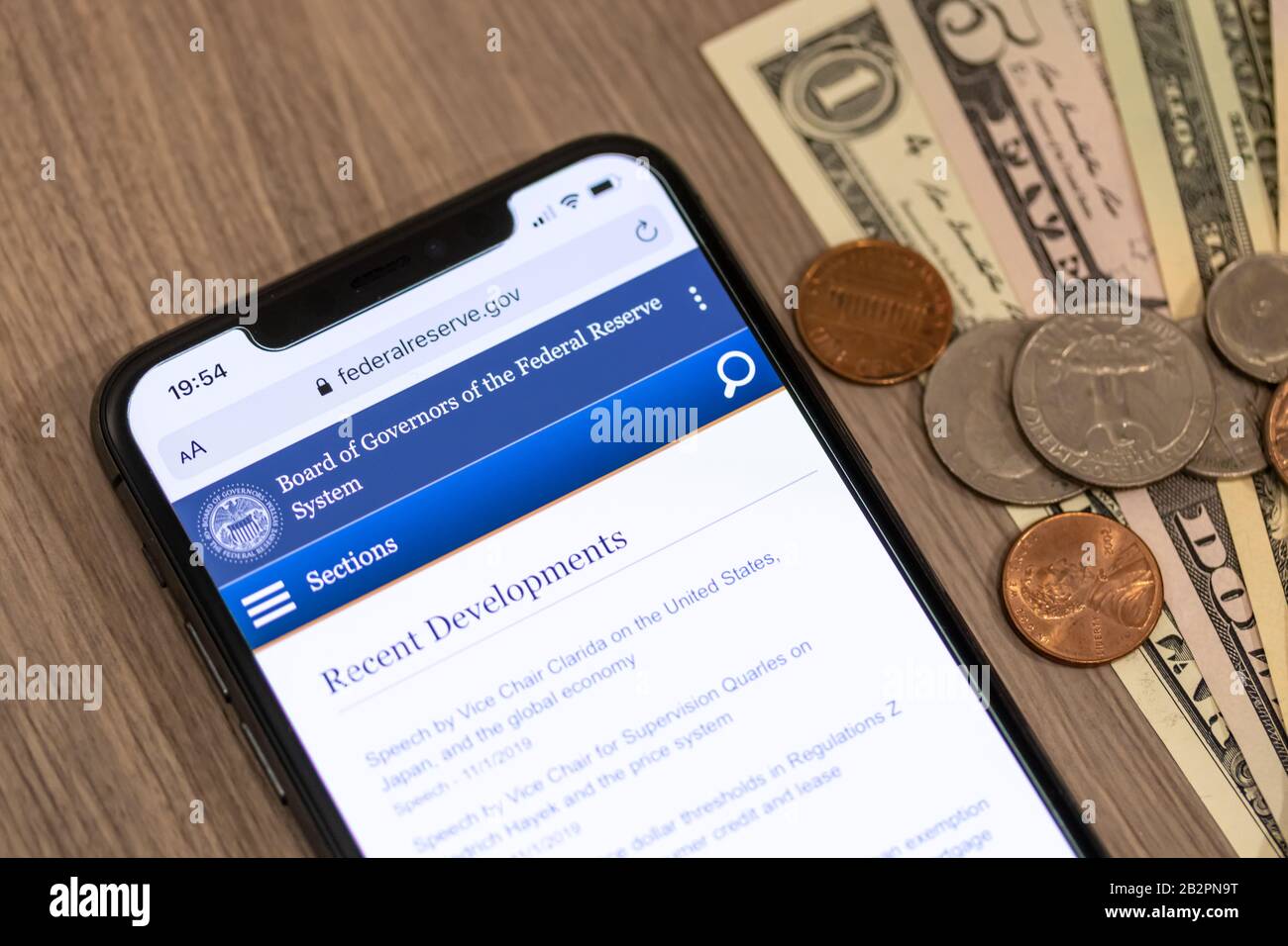 Sigillo e testo della Federal Reserve degli Stati Uniti in cima al loro sito web su uno smartphone accanto a una pila di contanti americani e cambio su una scrivania. Foto Stock