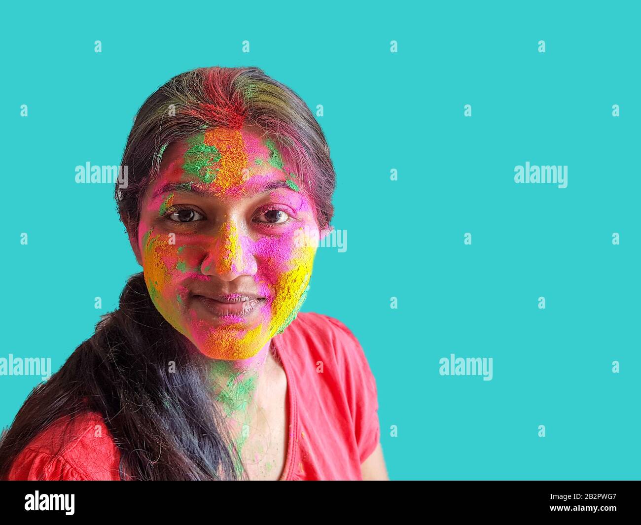 ritratto di una giovane signora con holi colori sorridenti alla fotocamera con isolato solido sfondo ciano. Foto Stock