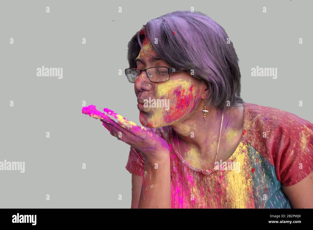 ritratto di una giovane signora con holi colori sul viso che soffia un bacio volante con isolato solido sfondo grigio. Foto Stock