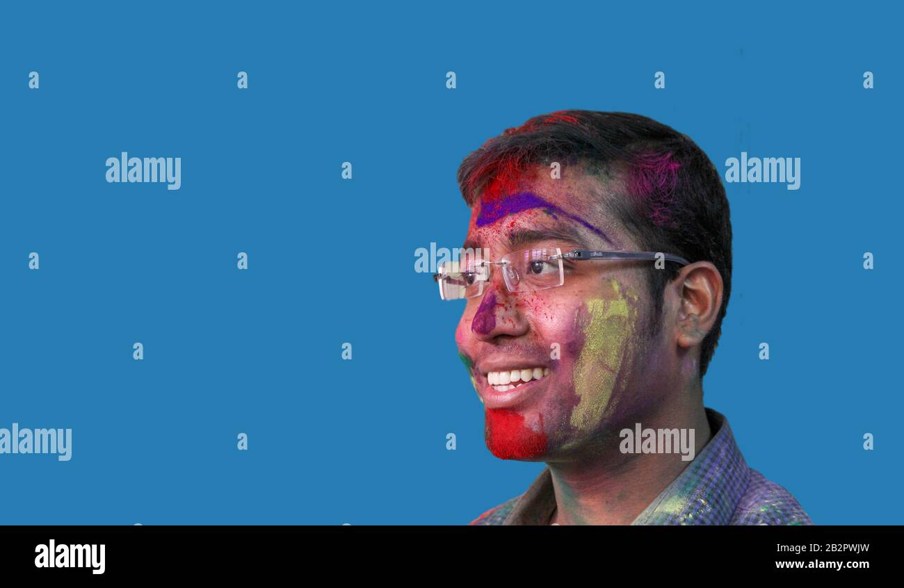ritratto laterale di un giovane uomo con holi colori sul viso sorridente a con isolato cielo solido sfondo. Foto Stock