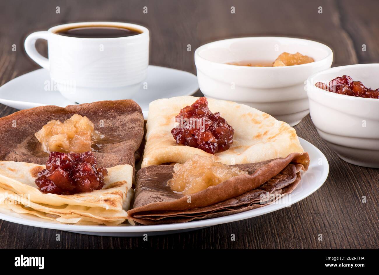 I pancake sono semplici e con cacao. Frittelle su un piatto bianco, marmellata di mele di diverse varietà e caffè su uno sfondo di legno. Russia Tradizionale Foto Stock