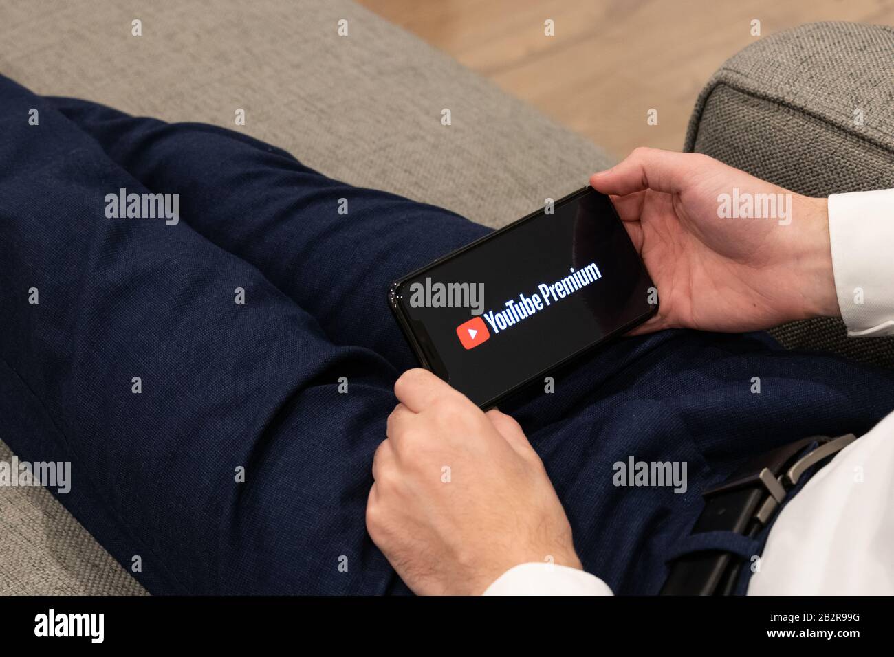 Uomo seduto su un divano che tiene un iPhone mentre il logo YouTube Premium è sullo schermo. Foto Stock