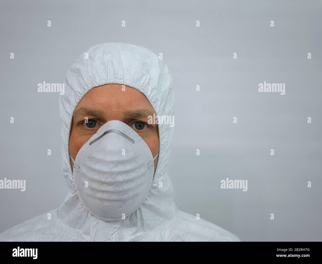 Un uomo che indossa una maschera protettiva e una tuta con cappuccio bianca Foto Stock