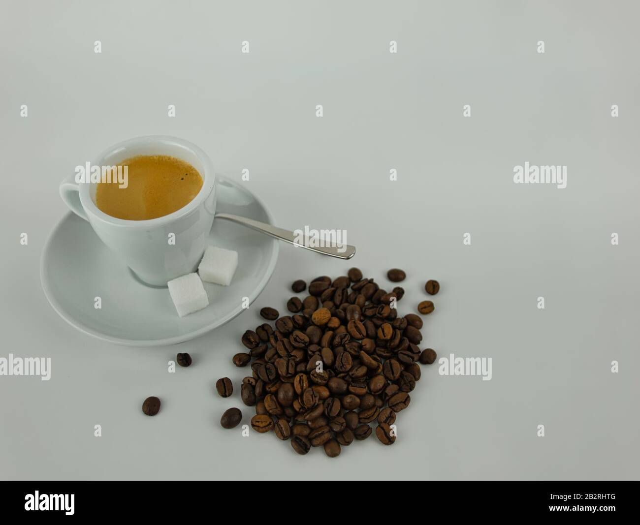 Una tazza di caffè con piattino e cucchiaio accanto a chicchi di caffè interi Foto Stock