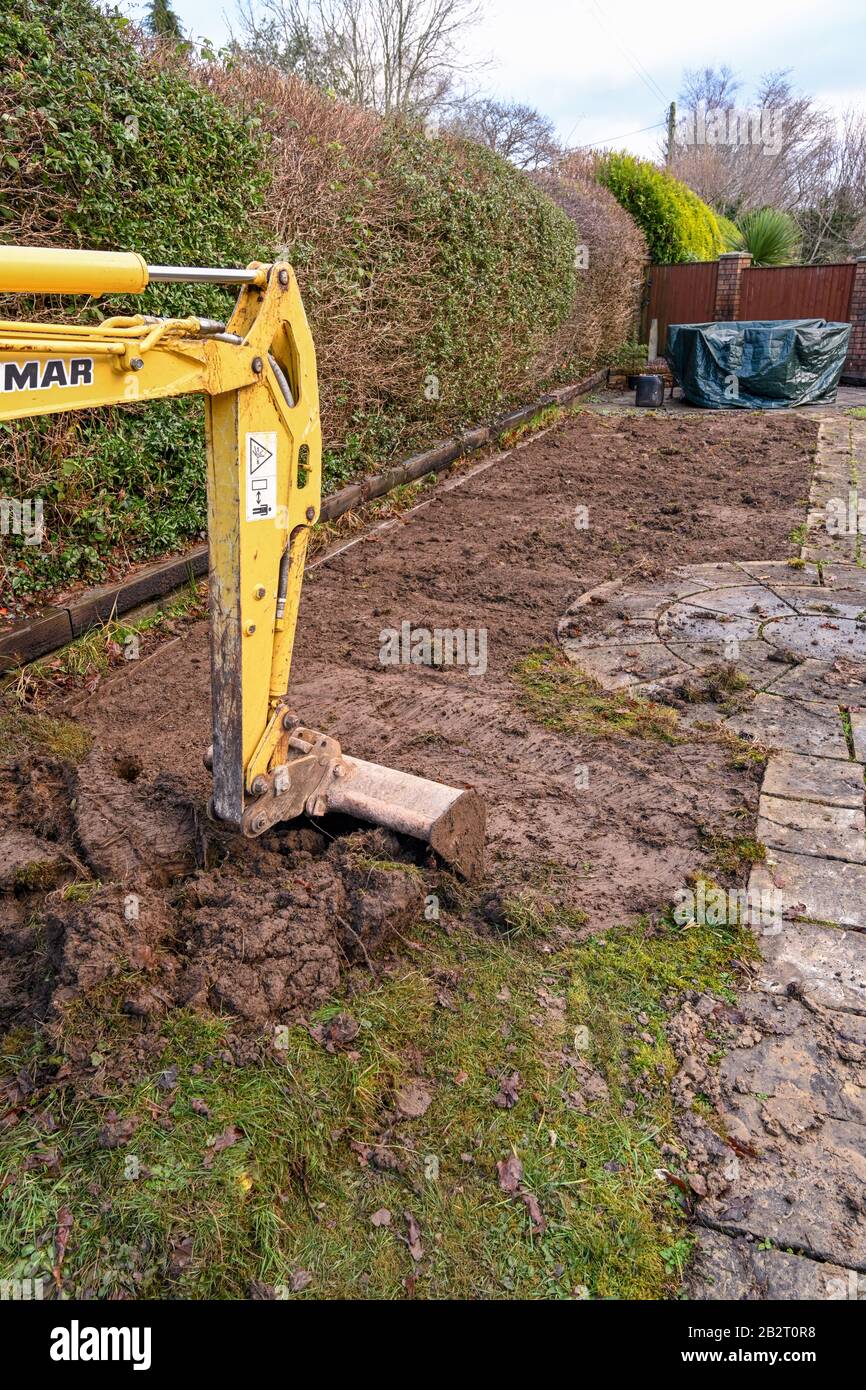 Cardiff, GALLES - GENNAIO 2020: Benna e braccio di un miniescavatore scavando il prato nel giardino posteriore di una proprietà residenziale Foto Stock