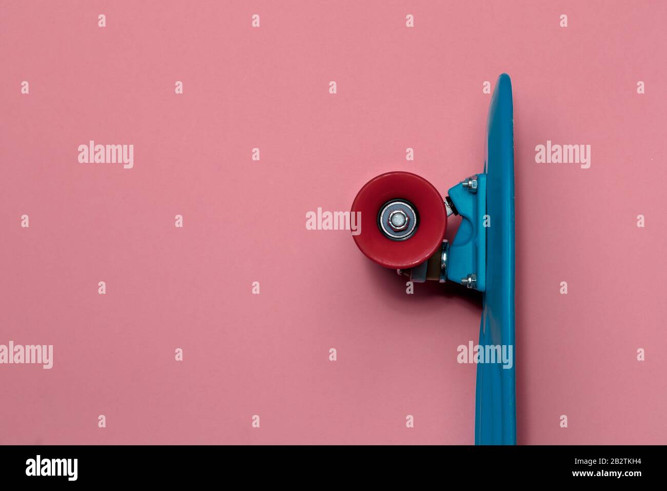 Crociera con skateboard blu con ruote rosse su sfondo rosa con spazio di copia Foto Stock