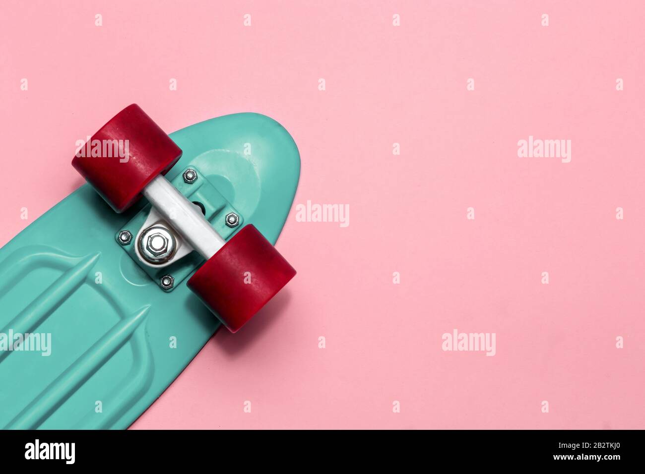 Crociera con skateboard verde con ruote rosse su sfondo rosa con spazio di copia Foto Stock