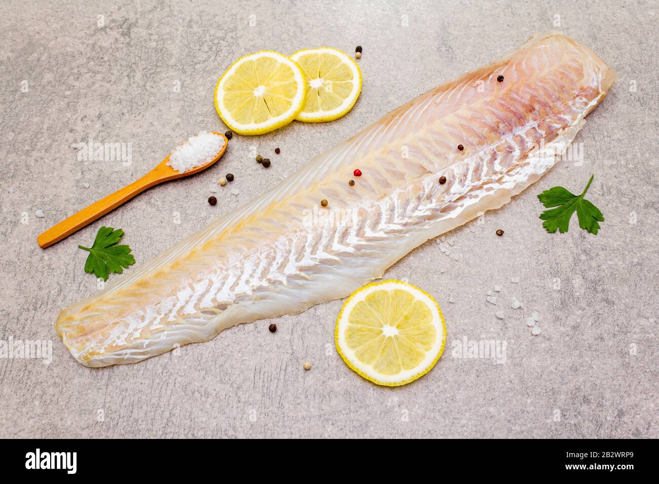 Filetto di nasello fresco crudo su fondo di pietra. Con limone, prezzemolo, sale in cucchiaio di legno e peperoni mescolare. Foto Stock