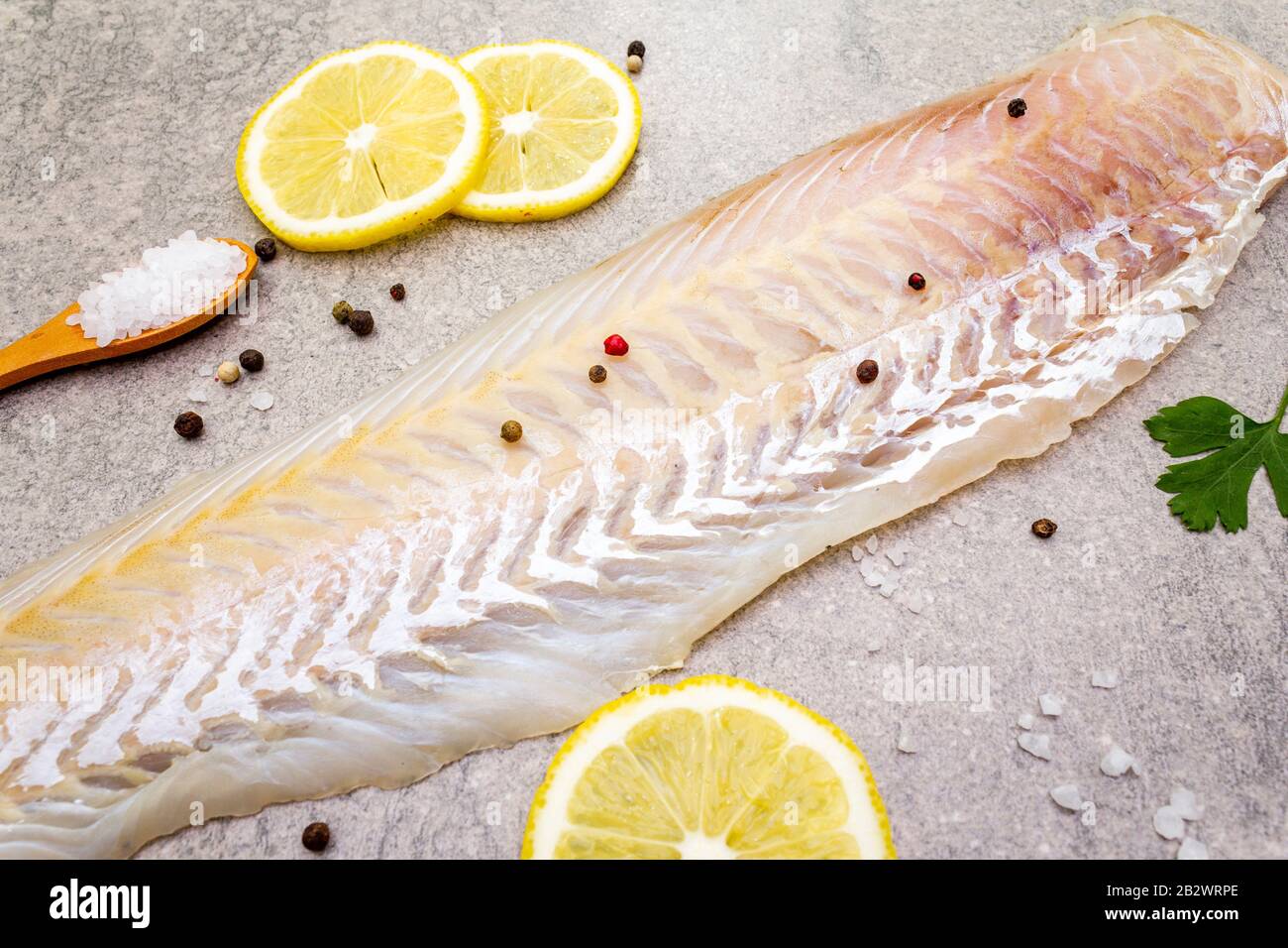Filetto di nasello fresco crudo su fondo di pietra. Con limone, prezzemolo, sale in cucchiaio di legno e peperoni mescolare. Primo piano. Foto Stock