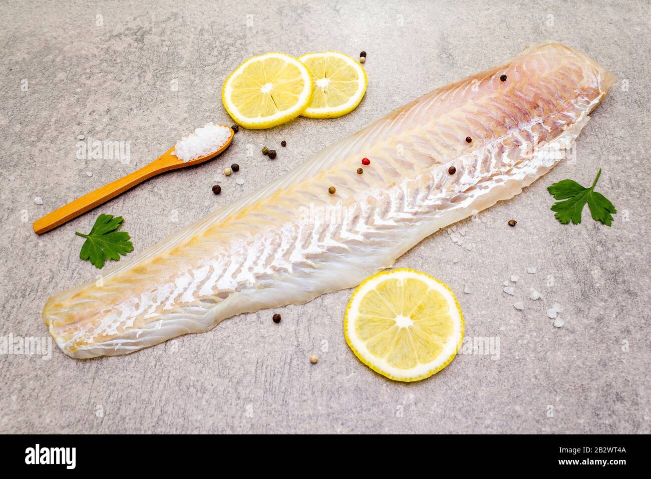 Filetto di nasello fresco crudo su fondo di pietra. Con limone, prezzemolo, sale in cucchiaio di legno e peperoni mescolare. Foto Stock