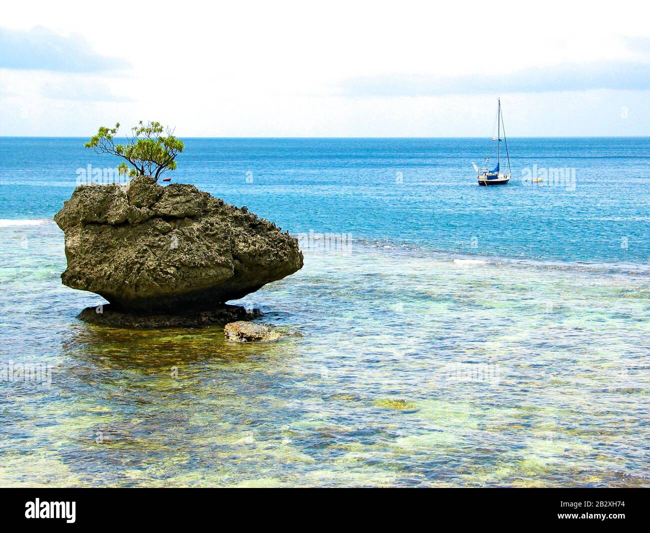 Un albero su una roccia e una piccola barca a vela ancorata, vista mare da Christmas Island, Oceano Indiano, territorio Australia. Foto Stock
