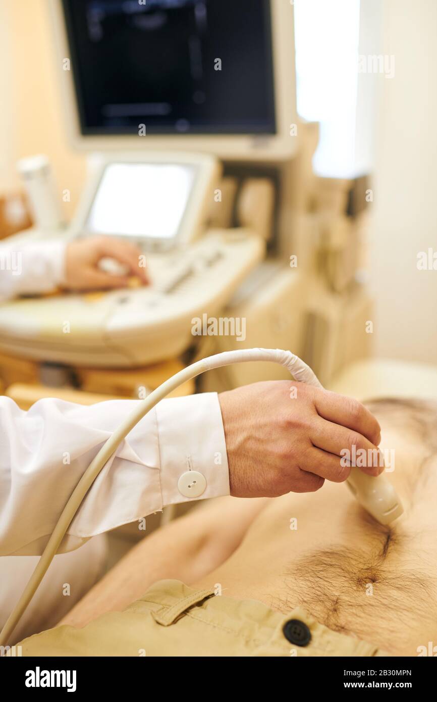 Primo piano del medico non riconoscibile utilizzando la sonda del trasduttore sulla pancia del paziente durante l'esame a ultrasuoni dello stomaco Foto Stock