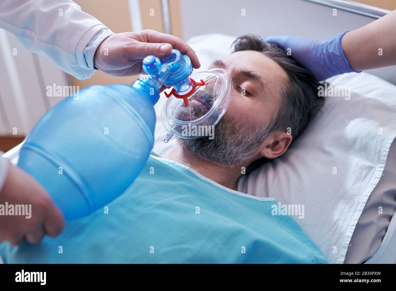 Primo piano di un medico non riconoscibile che posiziona la maschera della valvola della sacca sulla faccia del paziente incosciente Foto Stock