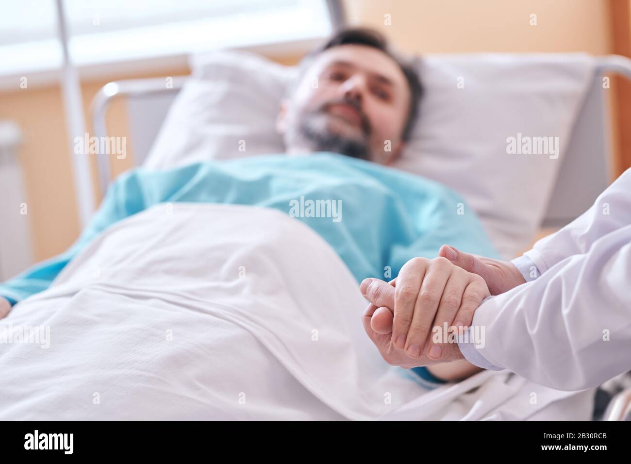 Primo piano di un medico irriconoscibile che tiene la mano del paziente mentre lo sostiene prima dell'intervento chirurgico Foto Stock