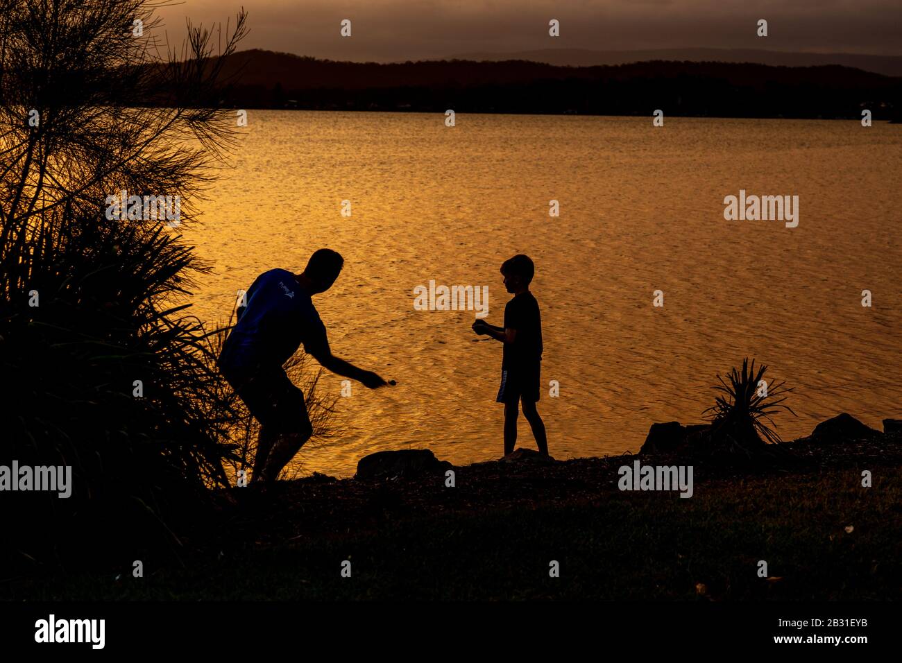 Tramonto sul lago Macquarie NSW Australia padre e figlio saltando pietre Foto Stock