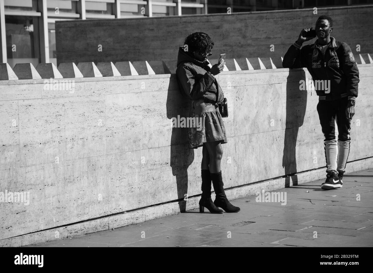 Roma, Italia. 23 Febbraio 2020. Un uomo nero e una donna nera con il loro smartphone. L'uomo sta parlando al telefono, la donna sta chiacchierando. Nero e. Foto Stock