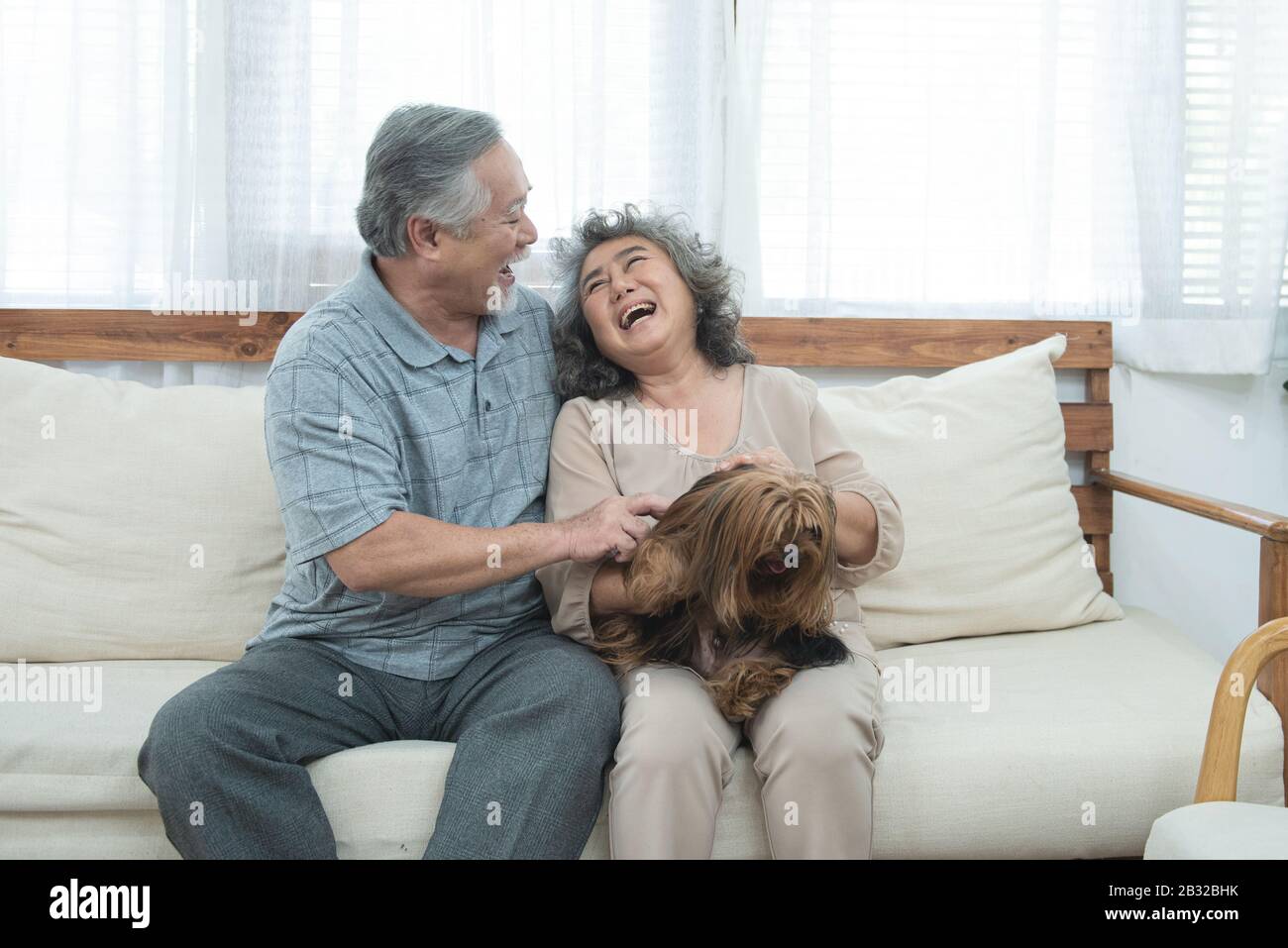 Felice anziano senior coppia asiatica sedersi sul divano insieme con la terapia degli animali domestici in cura di giorno di cura di professione, uomo Pensionato e donna che tiene il cane mentre si siede sul divano dentro Foto Stock