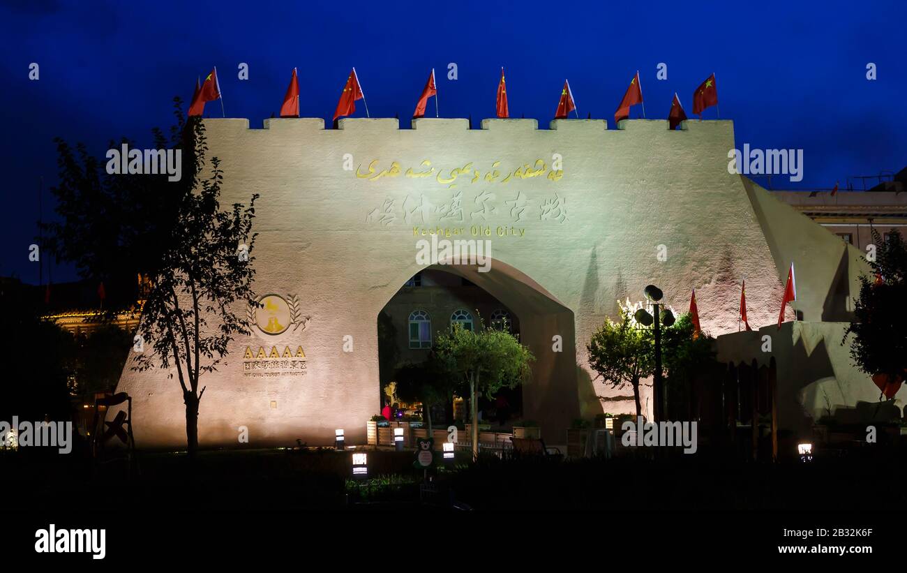 Porta della città al centro storico di Kashgar di notte. Sotto il cielo scuro e blu. Le bandiere cinesi sono montate sulla parte superiore del cancello illuminato (festa nazionale cinese). Foto Stock