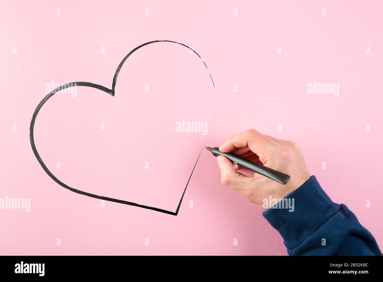 mano che disegna la forma del cuore usando penna di punta di feltro sullo sfondo rosa, amore e concetto di affetto Foto Stock