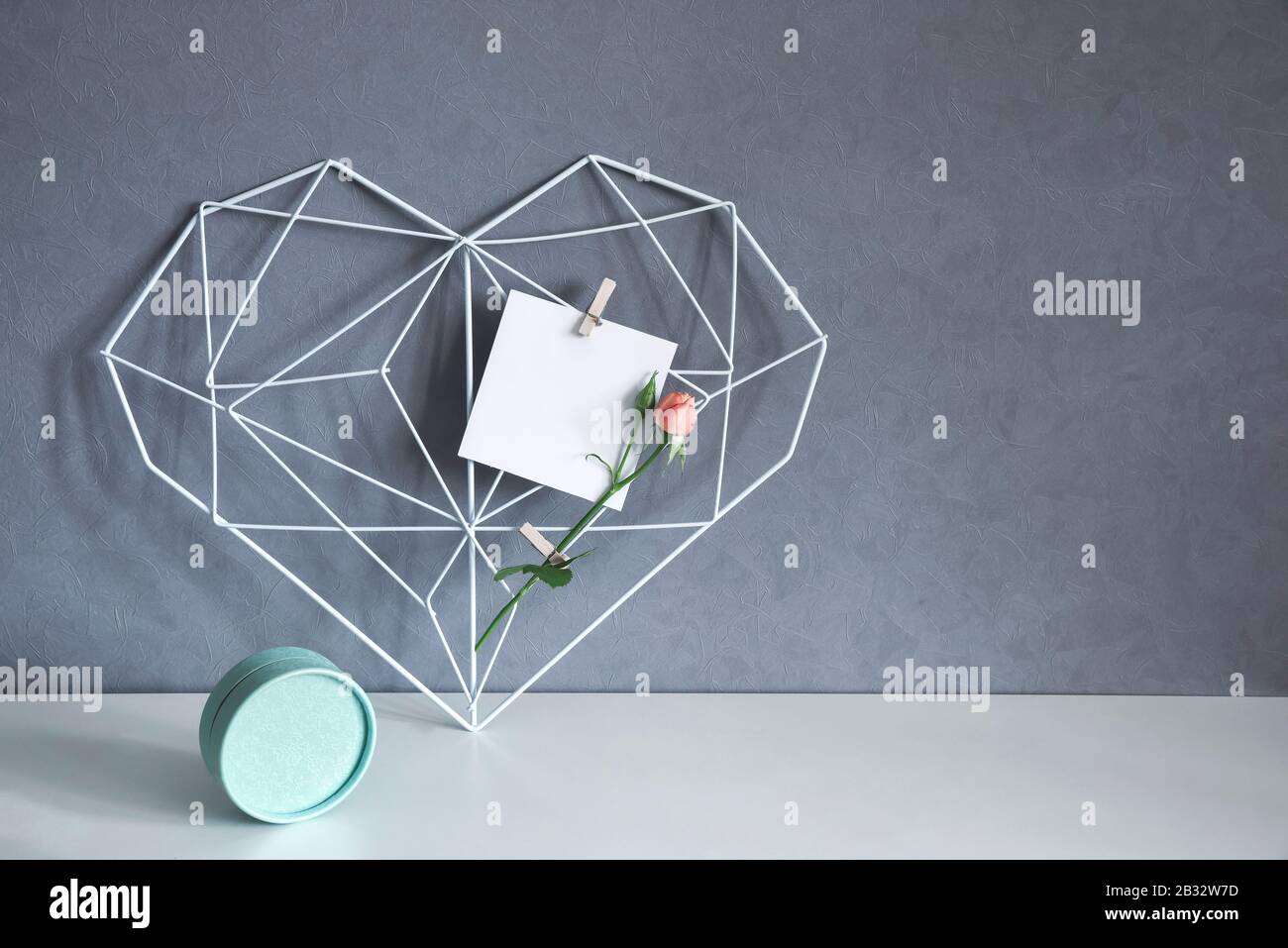 Struttura moderna a forma di cuore con fiore di rosa su sfondo grigio parete. Arredamento interno Simbolo Cuore di amore Foto Stock