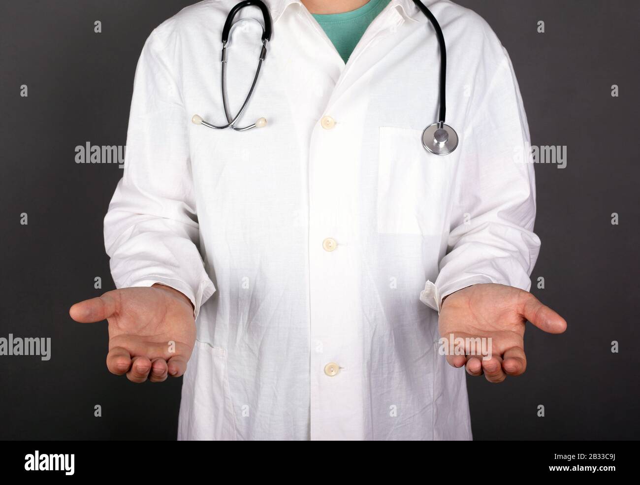 il medico in un cappotto bianco con uno stastoscopio su uno sfondo scuro allungare le mani e le palme copiare spazio. Foto Stock
