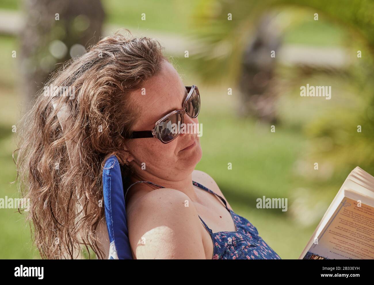 Giovane donna con i capelli lunghi e gli occhiali da sole si sedette al sole leggendo un libro, Gran Canaria, Gran Canarie, Spagna Foto Stock