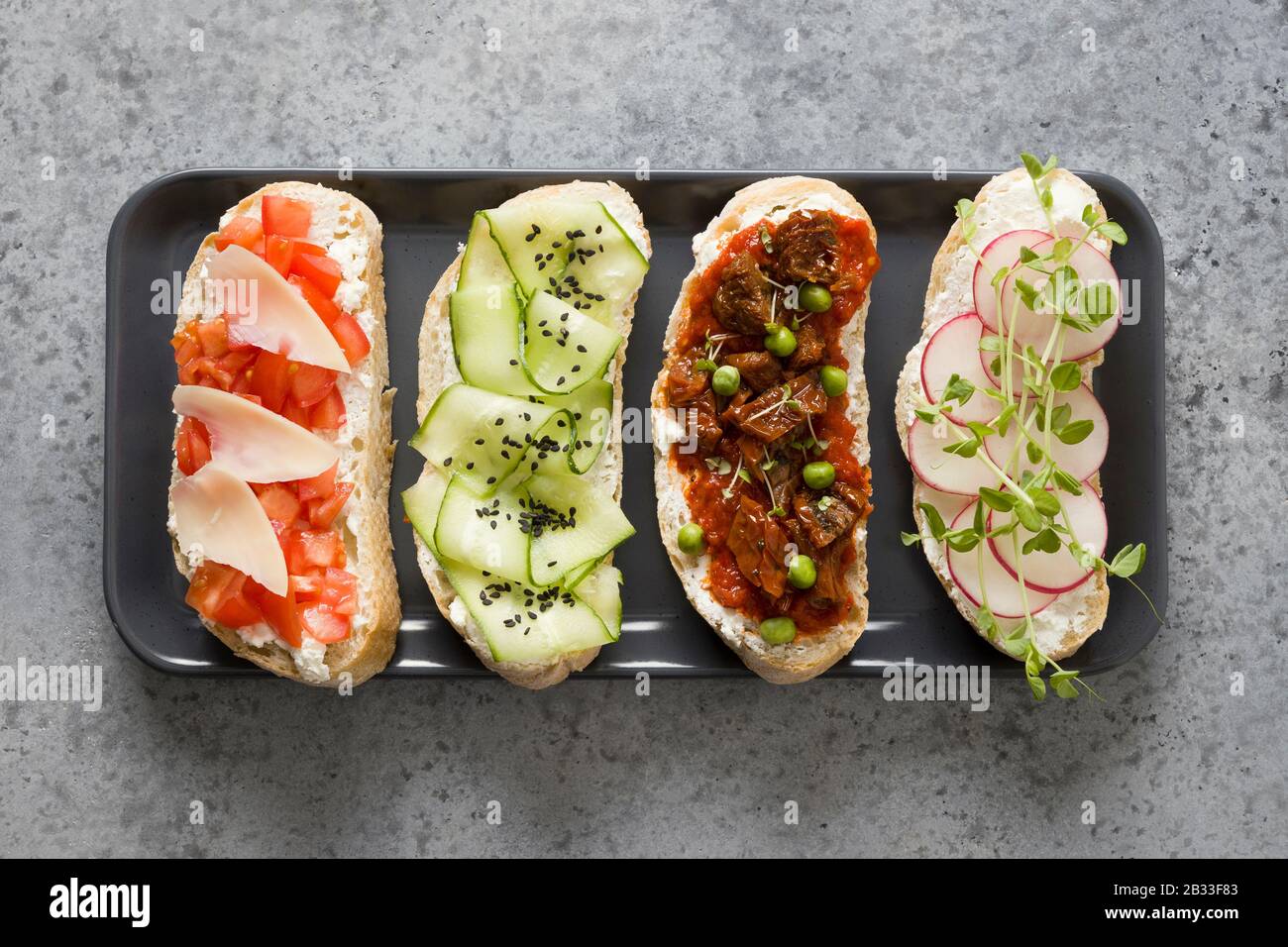 Panini su toast di ciabatta con verdure fresche, ravanelli, pomodori, cetrioli e microgens su sfondo grigio. Vista dall'alto. Foto Stock