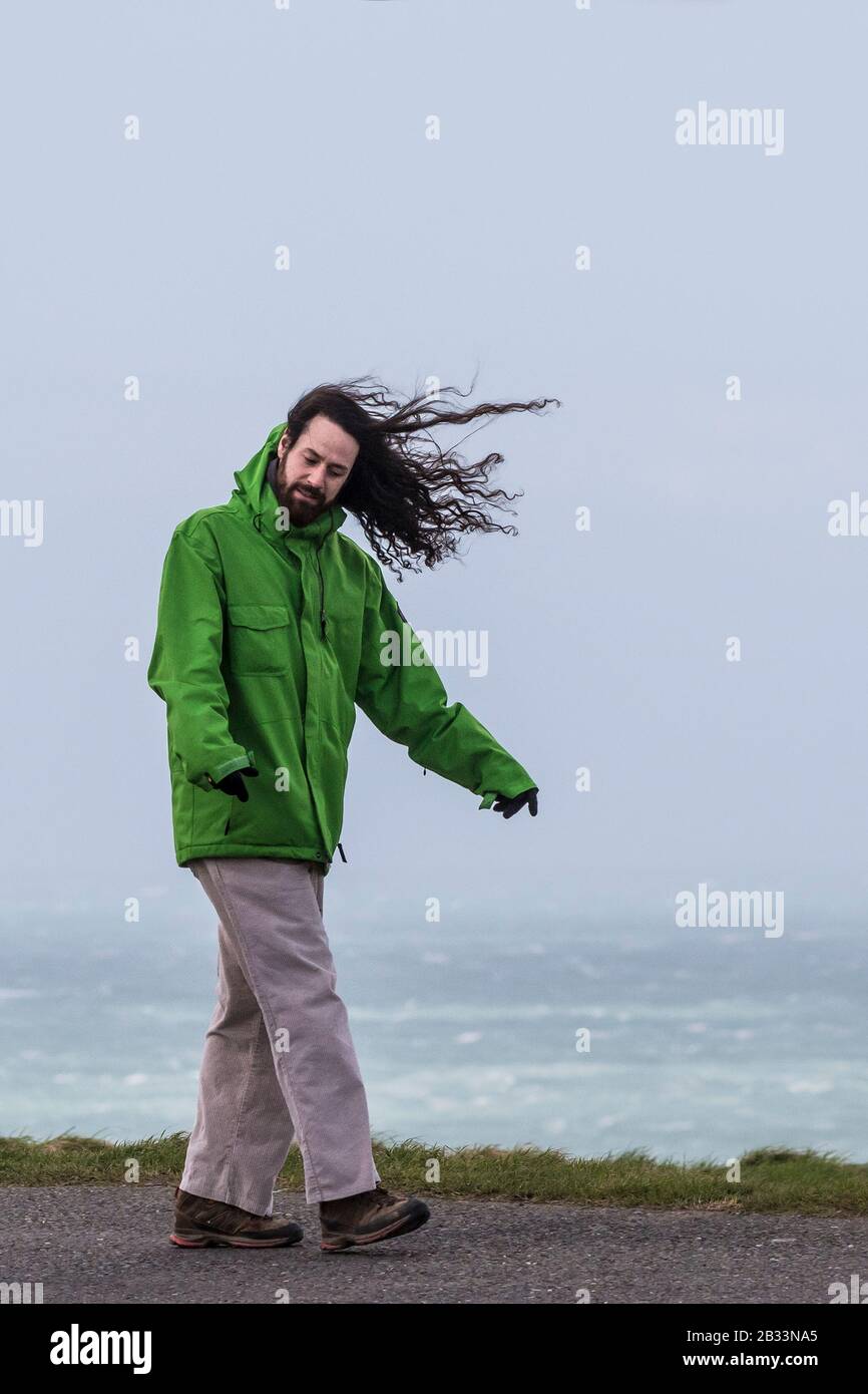 Un uomo con capelli lunghi che camminano in vento molto forte. Foto Stock
