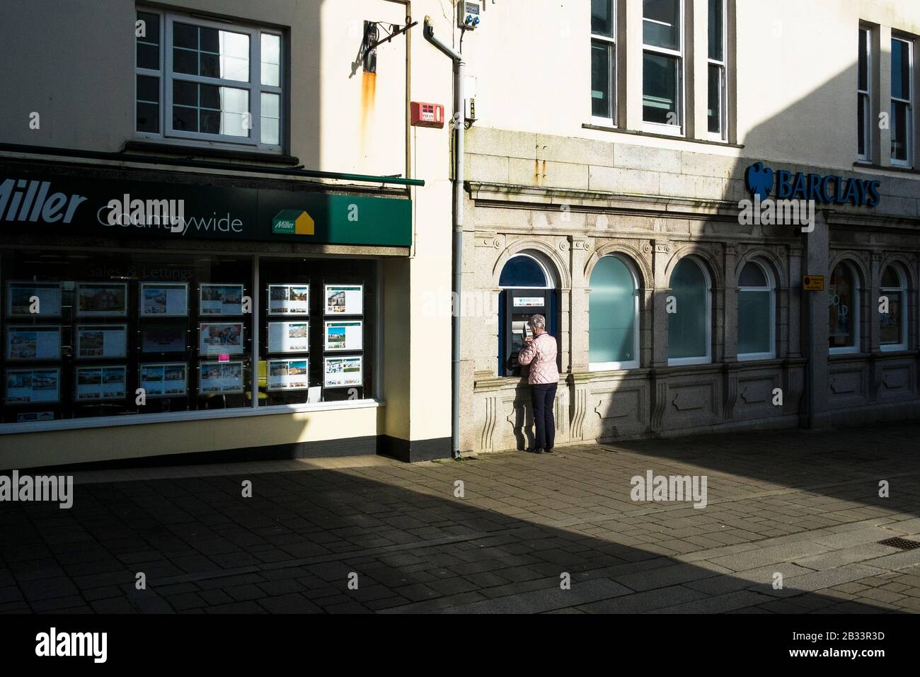 Un cliente che utilizza un bancomat presso una Barclays Bank al sole del pomeriggio nel centro città di Wadebridge in Cornovaglia. Foto Stock