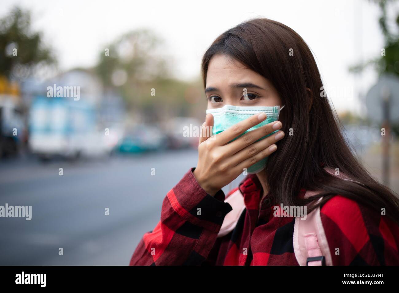 Asian giovane donna che cammina in città indossando maschera facciale a causa di inquinamento atmosferico, particolati e per la protezione del virus influenzale, influenza, coronavirus Foto Stock