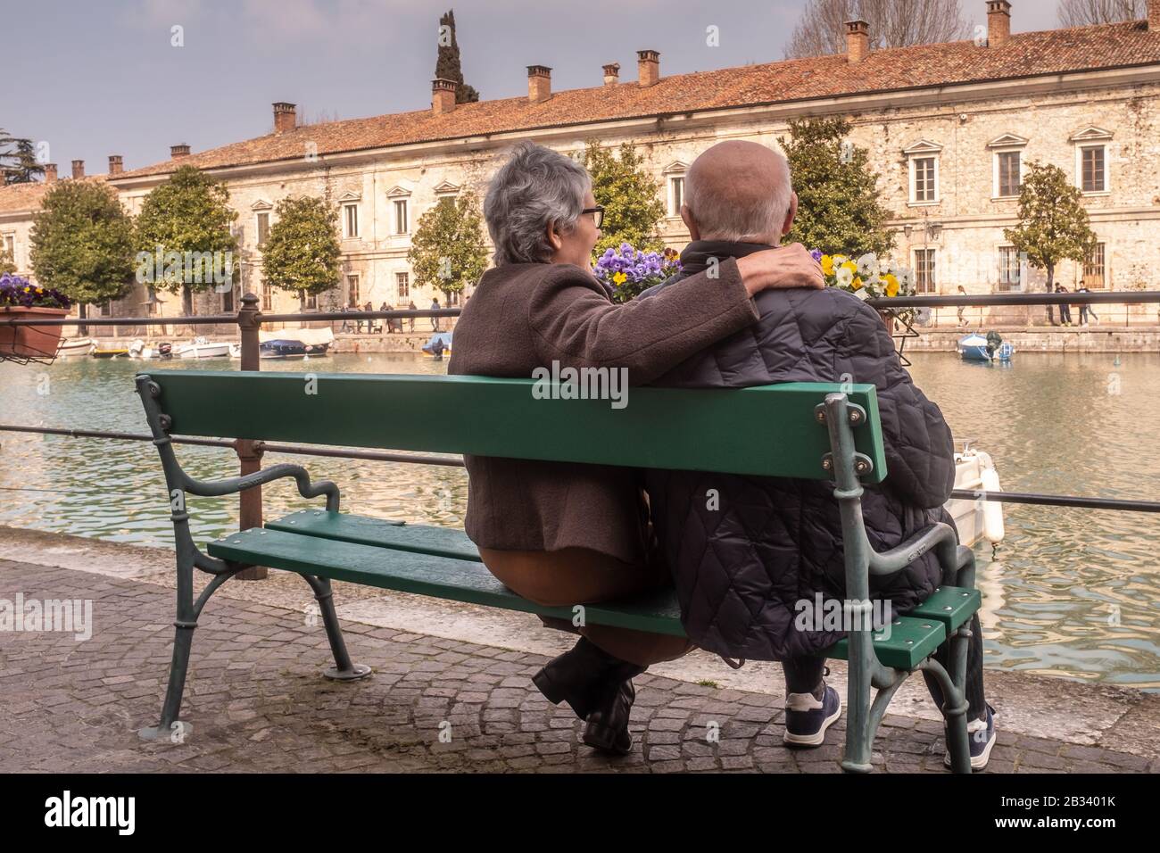Vista posteriore di una donna anziana abbracciando suo marito e guardando il pittoresco paesaggio con lui. Un momento di relax per una vecchia coppia. Foto Stock