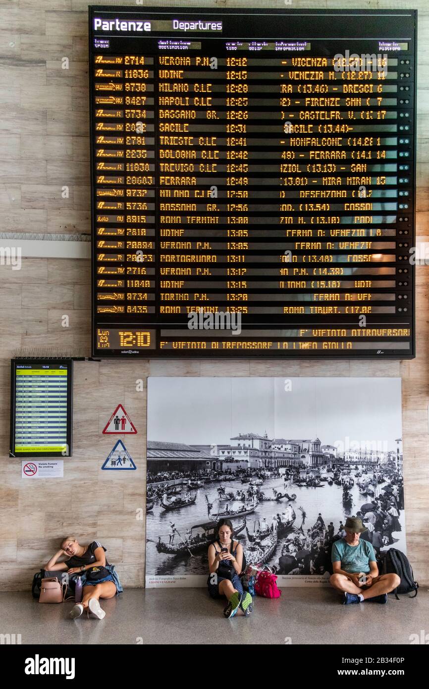 I turisti dormono e sui loro telefoni mentre aspettano all'interno della stazione ferroviaria Venezia Santa Lucia Venezia, Italia Foto Stock