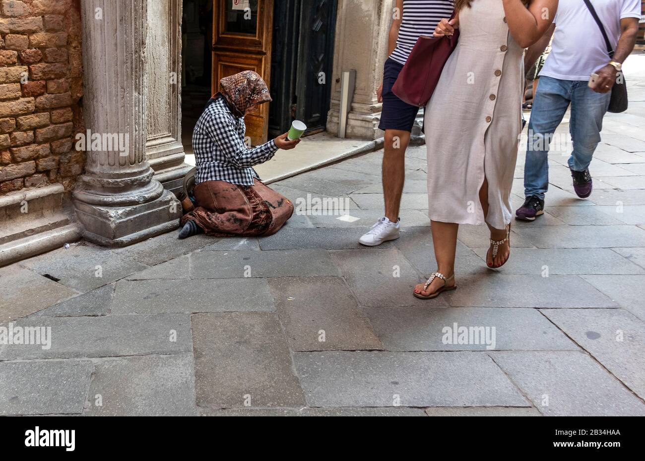 Donne che implorano per le strade di Venezia, Italia, mentre turisti passano ignorando Foto Stock