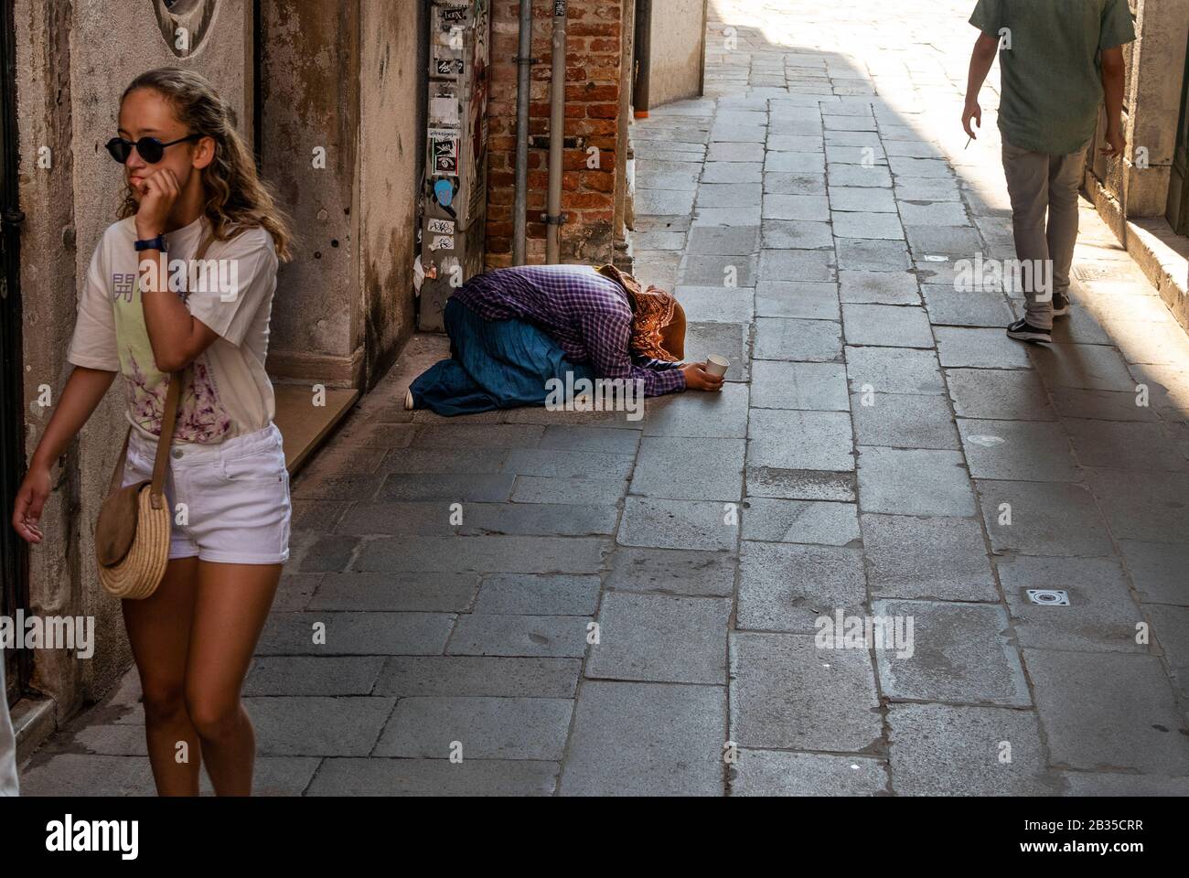 Turisti che camminano da donne che implorano per le strade di Venezia, Italia Foto Stock